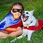 child dressed as a superhero with arm dog wearing a cape